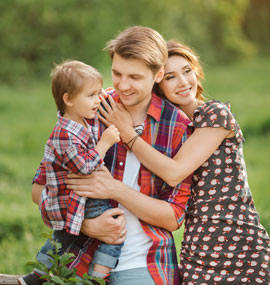 A young family with a father, mother and child standing outside in the day.
